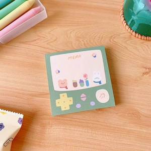 Detail of green retro game console memo pad with cute bear illustration on wood desk