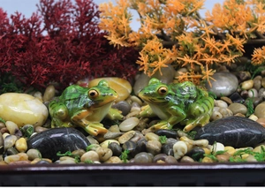 Detail of realistic green resin frog figurines placed on natural pebbles and green moss