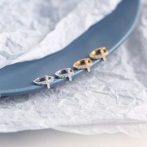 Detail of silver and gold cross hoop earrings with cubic zirconia on a blue plate