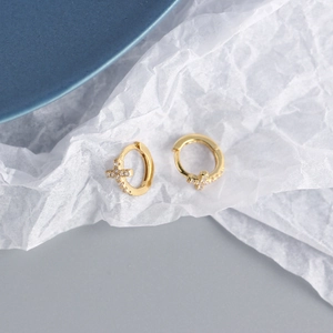 Macro shot of gold-plated cross earrings with shimmering zircon stones on textured paper