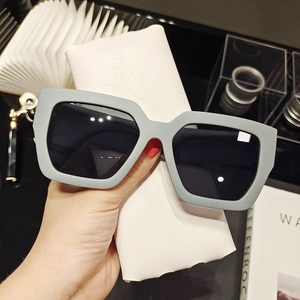 Detail of grey matte oversized square sunglasses held against a white leather pouch