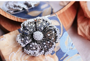 Close-up of vintage flower brooch with hollow silver design and white pearls on wooden base