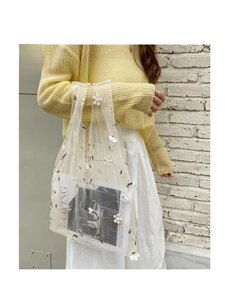 Close-up of white mesh handbag with delicate floral embroidery and magazine inside