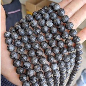 Detailed close-up of natural dark Larvikite round beads held in hand for jewelry making