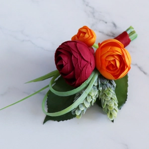 Artificial ranunculus boutonniere with red roses and greenery for groom wedding attire