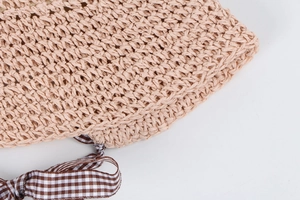 Close-up of woven straw texture and brown plaid ribbon bow on the sun hat brim