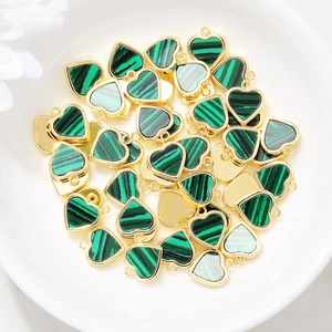 Golden heart charms with green malachite stone in a white ceramic dish for DIY jewelry