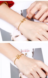 Detail of a gold box chain bracelet with a 3D letter M pendant and heart charm detail