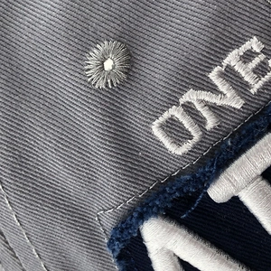 Gros plan de la broderie ONE et de l'œillet cousu sur la casquette en sergé gris