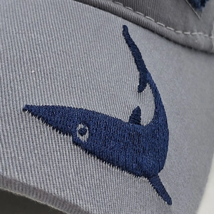 Détail macro de la broderie de requin bleu marine sur une casquette en coton gris