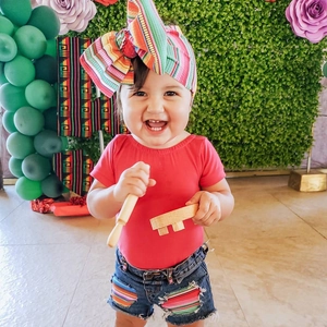 Smiling toddler wearing a colorful striped bow headband at a festive party scene
