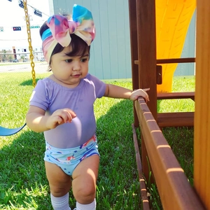 Detail of baby in purple romper and blue printed shorts with rainbow tie-dye bow headband