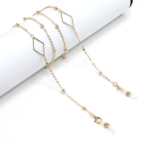 Fashionable gold glasses chain with geometric diamond charms and small beads on a white stand