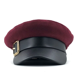 Detail of burgundy wool baker boy hat with black faux leather visor and gold metal buckle