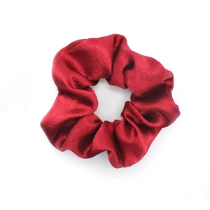 Detailed close-up of a deep red satin scrunchie with elegant pleated fabric texture