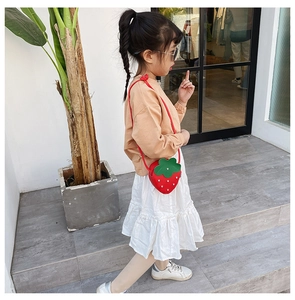 Detailed side view of a young girl wearing the red strawberry-shaped crossbody bag