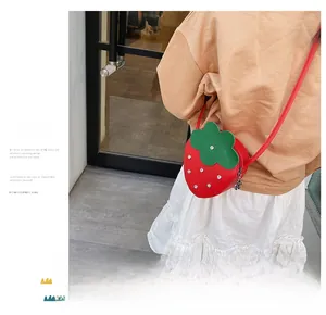 Detail of red strawberry shaped crossbody bag with silver rivets and cute bear pendant