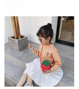 Detail of red strawberry-shaped crossbody bag paired with a cream long-sleeved shirt