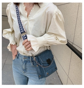 Blue crossbody bag with black heart detail and jacquard strap shown on model outdoors