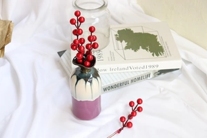 Modern white ceramic vase with vibrant red artificial berries on white fabric