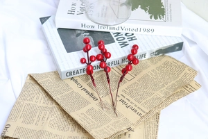 Close-up of three artificial red berry stems on a white linen cloth with newsprint decor