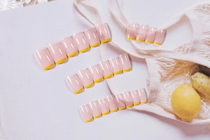 Flat lay of 24pcs long coffin press-on nails in nude pink with bright yellow French tips