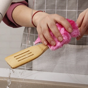 Microfiber pink cleaning cloth washing a bamboo spatula in a bright kitchen setting
