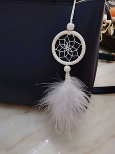 Close-up of white dreamcatcher keychain with soft feathers and beads on a blue bag