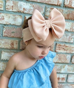 Detailed close-up of a large pink waffle knit bow headband on a young child