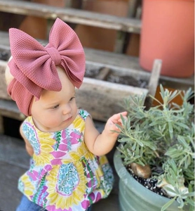 Close-up of baby girl wearing oversized dusty pink waffle knit bow headband in outdoor setting
