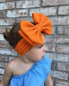 Close-up of an orange waffle-knit oversized bow headband on a young child
