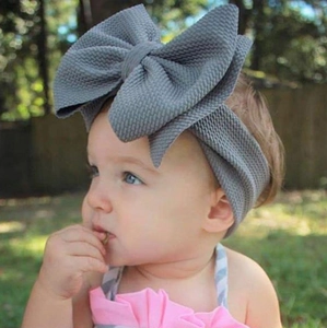 Close-up of a grey waffle knit baby headband featuring an oversized bow on an infant