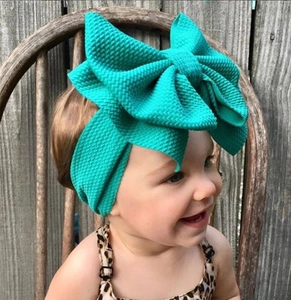 Close-up of baby girl wearing a large teal waffle textured bow headband on a vintage chair