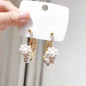 Detailed shot of pearl cluster hoop earrings in warm gold held on jewelry display card