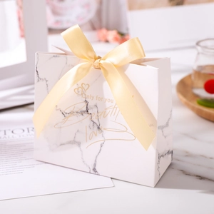 Macro detail of white marble pattern gift bag with champagne gold silk ribbon bow