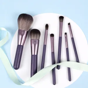 Detail view of 7 purple makeup brushes with soft bristles on a white platform