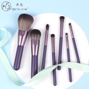 Detail view of 7 purple makeup brushes with soft bristles on a white platform