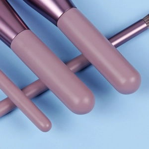 Close-up of portable purple makeup brushes with soft bristles and metal ferrules on blue background