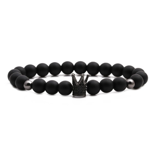 Matte black stone beaded bracelet with crown charm and metal spacers on white background