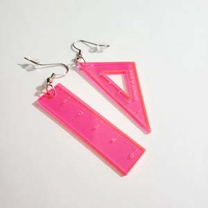 Macro detail of pink acrylic ruler earrings with silver hooks and school theme prints