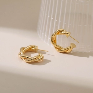 Polished 18K gold plated twisted C-shape hoop earrings on minimalist stone display