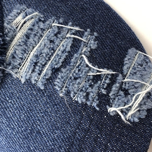 Macro detail of distressed dark blue denim with torn edges and white stitching