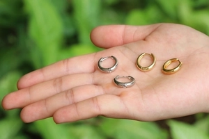 Minimalistische U-förmige Creolen in Gold und Silber auf der Hand vor Gartenhintergrund
