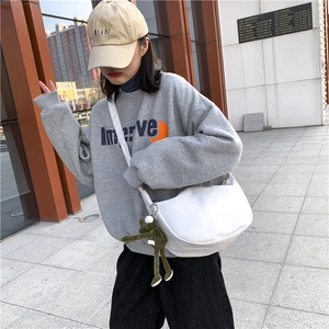White canvas messenger bag with a green frog plush charm worn by a model outdoors