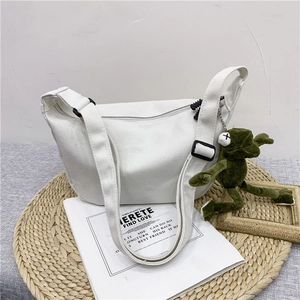 Detailed view of white canvas crossbody bag with cute green frog plush charm accessory