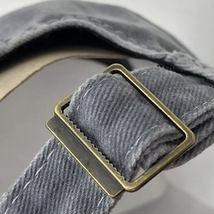 Macro detail of the adjustable bronze metal buckle on the dark grey vintage cotton army cap
