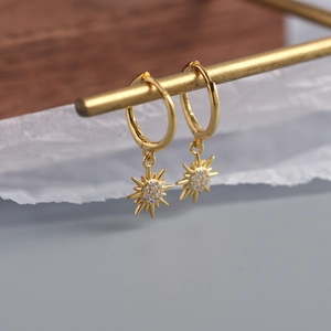 Macro shot of gold sunburst hoop earrings with sparkling zircon star pendants