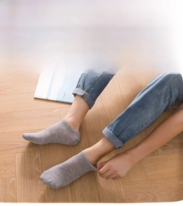 Close-up of comfortable light grey low-cut cotton socks worn on a wooden floor