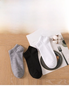 Flat lay of gray black and white invisible low cut socks on wooden floor with kinfolk magazine