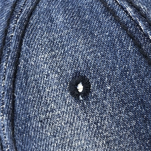 Dettaglio del tessuto denim blu scuro con occhiello nero ricamato sulla parte del cappello